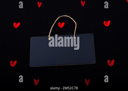 Rectangular shaped black notice board and red hearts on black background Stock Photo