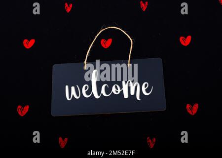 Welcome wording on black notice board with red hearts around Stock Photo