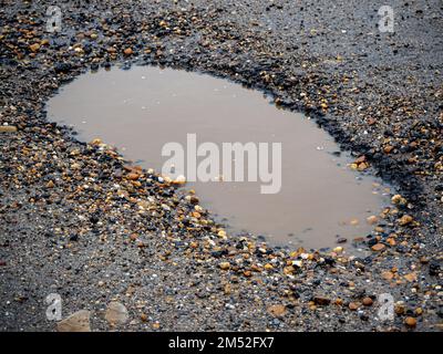 Pothole on a paved road on a rainy winter day. Concept of risk and traffic problems Stock Photo