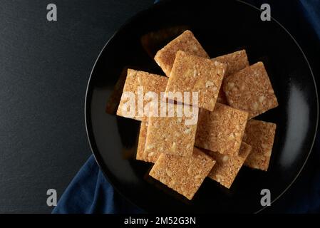 coconut biscuits on black plate, served textured crispy square shaped homemade cookies on a table top , taken from above with copy space Stock Photo