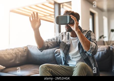 Right where the action is. a young man using a virtual reality headset on the sofa at home. Stock Photo