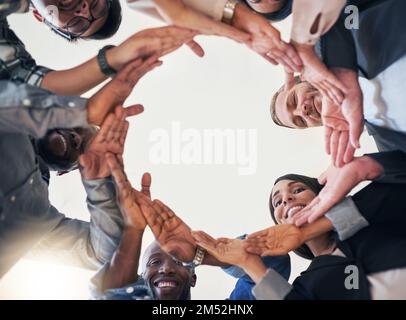 Keeping the creativity flowing. Low angle shot of a team of creative colleagues making a circle with their hands in the office. Stock Photo