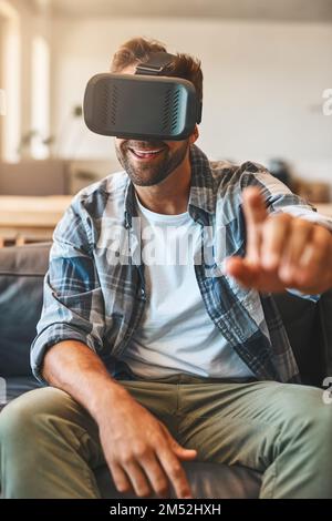 Youve gotta feel it to believe it. a young man using a virtual reality headset on the sofa at home. Stock Photo