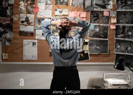 Detective looking at evidence board in her office, back view. Copy space Stock Photo