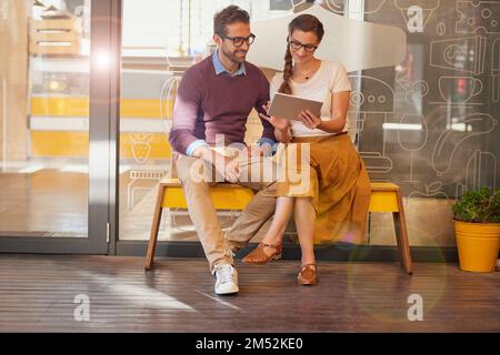 These specials are sure to draw customers to our shop. two happy young business owners using a tablet together while sitting outside their coffee shop Stock Photo