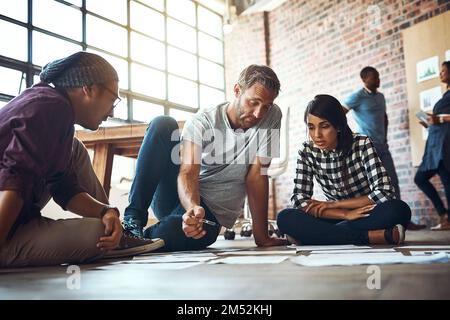 No team works without teamwork. a team of entrepreneurs collaborating and sitting on the floor in a modern office. Stock Photo