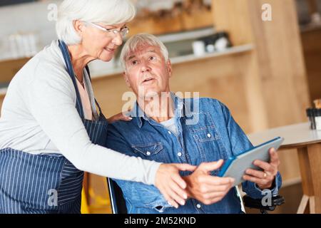 Let me show you, dear. two senior business owners looking at a tablet together while working in their coffee shop. Stock Photo
