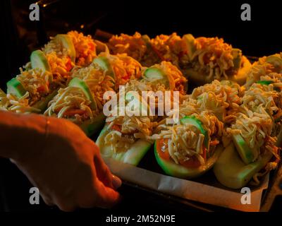 Stuffed zucchini with minced meat, tomatoes and cheese. Woman puts baking sheet with dish in oven for baking. Healthy food. Recipe delicious food at home. Stock Photo