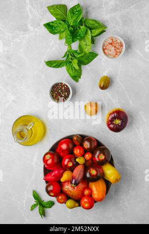 Vertical composition with various types of tomatoes, basil and spice on marble background Stock Photo