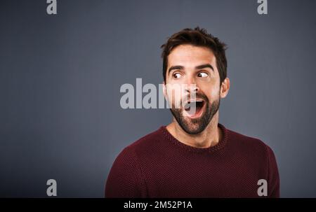 He cant believe what he just heard. Studio shot of a handsome young man looking surprised against a gray background. Stock Photo