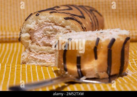 Strawberry sponge roll cake with whipped cream, jam and chocolate. On a yellow check cloth Stock Photo