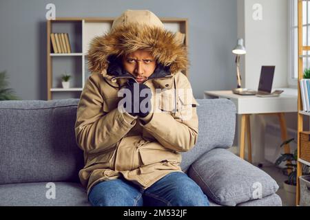 Young man freezing in cold winter and wearing coat inside house without central heating Stock Photo