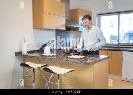 Senior white man cooking with a pan in hand in the kitchen at home. Stock Photo
