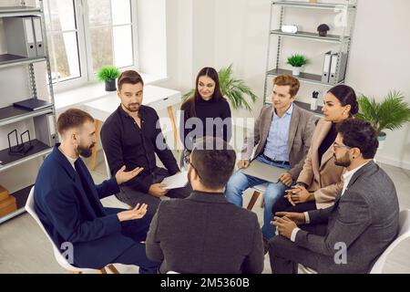 Male leader talking to group of office workers, brainstorming, discussing business strategy. Stock Photo