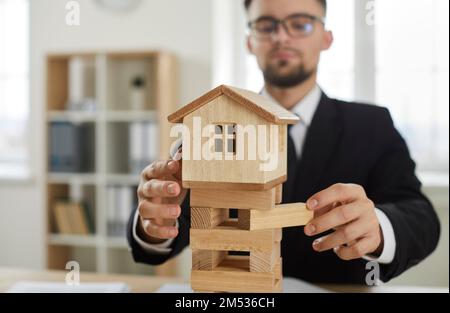 Business man removes blocks from under toy house as concept of unstable real estate market Stock Photo