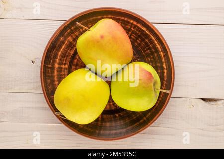 Three sweet green apples with a clay plate on a wooden table, macro, top view. Stock Photo