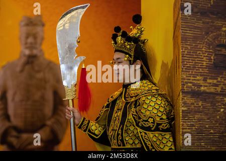 Moscow, Russia. 24th of December, 2022. A man dressed as an ancient Chinese warrior with a Guan Dao halberd on the background of an image of the Chinese terracotta army warrior in a museum of Moscow, Russia Stock Photo