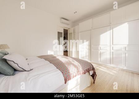 Double bedroom with queen size bed, wooden bedside tables, large balcony windows and white wall to wall fitted wardrobes and pine wood flooring Stock Photo