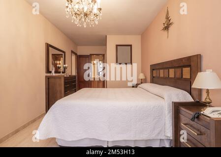 Bedroom with a double bed with a dark wood headboard and wooden bedside tables and chest of drawers with a matching mirror and access to an en-suite b Stock Photo
