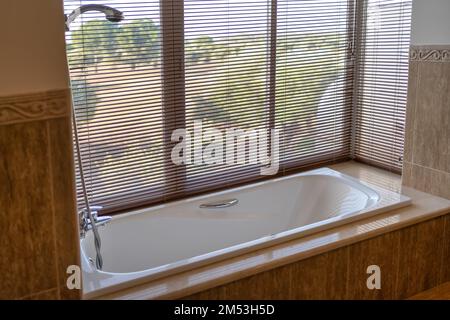 Apartment bathtub surrounded by glass overlooking the outside forest on a sunny day. Stock Photo