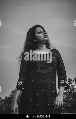 A vertical low-angle grayscale shot of an Indian woman wearing a traditional dress Stock Photo