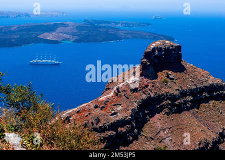 An aerial horizontal view from a cliff of Santorini island surrounded by Aegean Sea and a white boat Stock Photo