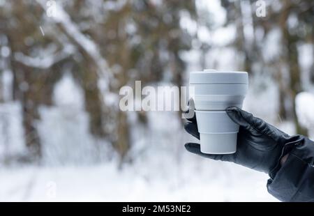 Hand in glove holding takeaway eco coffee cup, takeout tea mug on winter holidays, background for text. High quality photo Stock Photo