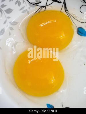 Potrait veiw two yellow yolk chicken eggs in a white bowl. Stock Photo