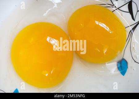 Two bright yellow yolk chicken eggs in a white bowl. Stock Photo