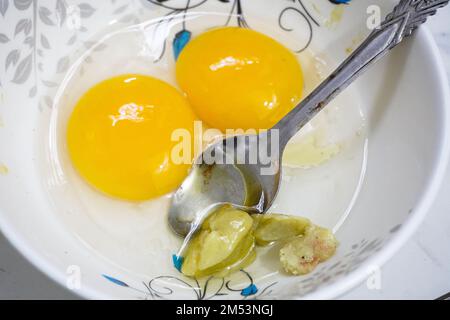 Top view of two raw eggs yolk in bowl with a steel spoon. Stock Photo