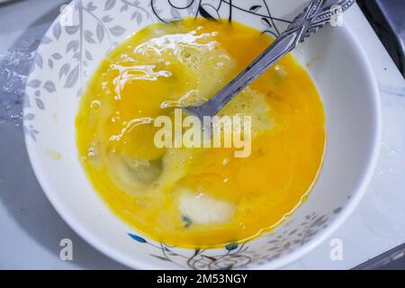 Top view of two raw eggs crucked yolk in bowl with a steel spoon. Stock Photo
