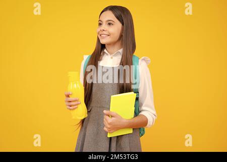 Teenager schoolgirl with backpack holding water bottle isolated on yellow background. Back to school concept. Healthy teen child. Stock Photo