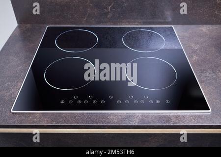 Grey countertop with black glossy built in ceramic glass induction or electric hob stove cooker with four burners in dark empty modern contemporary Stock Photo