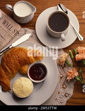 Overhead, still life shot of the table setting with Croissant on a platter, cup of coffee, flowers and the Wall Street Journal Stock Photo