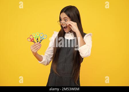 Teenage school girl with scissors, isolated on yellow background. Child creativity, arts and crafts, diy tools. Stock Photo