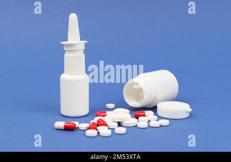 Medical concept. On a blue surface are white tablets and red-white capsules, an open container and a nasal spray. Stock Photo