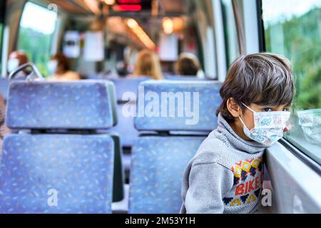 kid with face mask travelling in a train and looking out the window Stock Photo