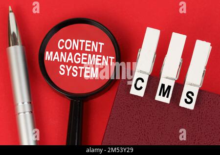 Business concept. On the red surface lies a pen, a notebook with clothespins - CMS, and a magnifying glass with the inscription - content management s Stock Photo