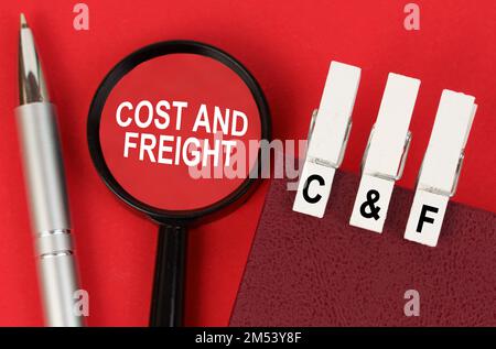 Business concept. On the red surface lies a pen, a notebook with clothespins - C and F, and a magnifying glass with the inscription - Cost and Freight Stock Photo