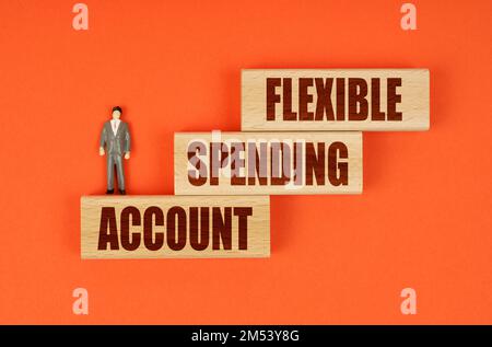 Business concept. On an orange surface on wooden blocks with the inscription - FLEXIBLE SPENDING ACCOUNT, there is a miniature figure of a businessman Stock Photo