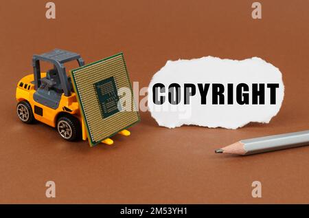 Technological concept. On a brown surface, a forklift is transporting a processor, next to it is paper with the inscription - Copyright Stock Photo