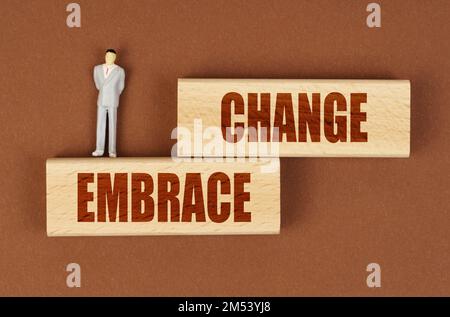 Business concept. On a brown surface on wooden blocks with the inscription - EMBRACE CHANGE, there is a miniature figure of a businessman. Stock Photo