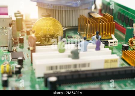 Business and technology concept. On the motherboard of the computer is a gold bitcoin coin and miniature figures of people. Figures out of focus. Stock Photo