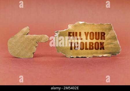 Industrial concept. On a brown surface, a cardboard hand points to a sign that says - Fill Your Toolbox Stock Photo