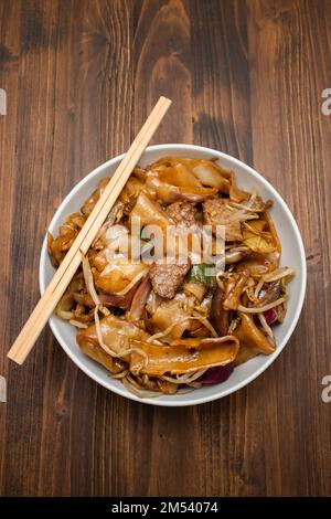 Fried noodles with vegetables and beef in white bowl on brown Stock Photo