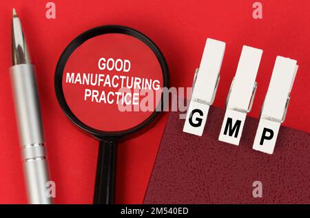 Business concept. On the red surface lies a pen, a notebook with clothespins - GMP, and a magnifying glass with the inscription - Good Manufacturing P Stock Photo