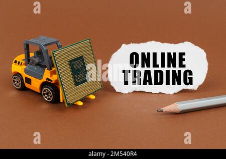 Technological concept. On a brown surface, a forklift is transporting a processor, next to it is paper with the inscription - Online trading Stock Photo