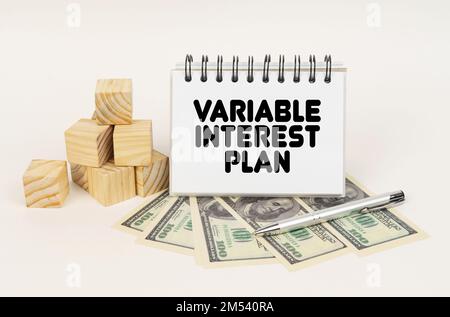 Business concept. On a white surface, cubes, dollars, a pen and a notepad with the inscription - Variable Interest Plan Stock Photo