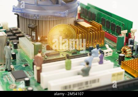 Business and technology concept. On the motherboard of the computer is a gold bitcoin coin and miniature figures of people. Figures out of focus. Stock Photo