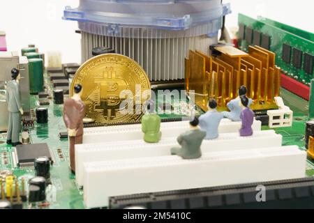 Business and technology concept. On the motherboard of the computer is a gold bitcoin coin and miniature figures of people. Figures out of focus. Stock Photo